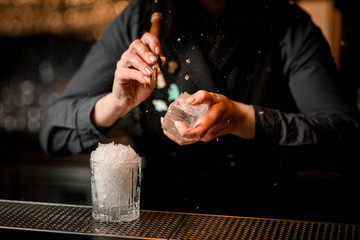 Woman bartender breaks large piece of ice with special instrument.