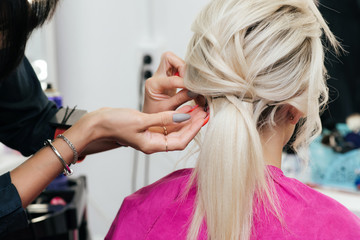 hands of a hair stylist with an invisible hairpin do the hair of a blonde girl with long hair