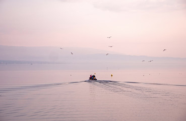 Fishermen leave to collect catches from pots. Sunrise over lake Geneva as the crew and their small boat head out from shore to check their morning catch.