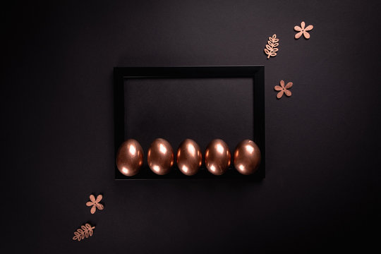 Easter background with black fhoto frame and gold Easter eggs on black background. Flat lay, Top view, mockup, copy space.
