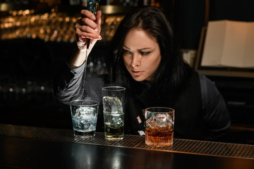 Woman bartender gently pours drink to glass with ice.
