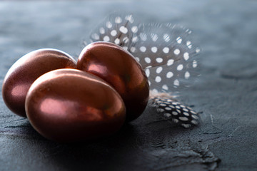 Golden egg and feather on dark background. Easter minimal background Copy space.