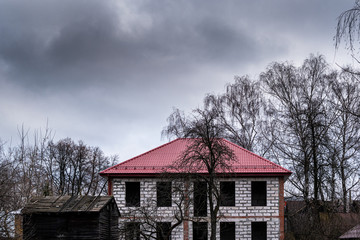 Abandoned unfinished house in the suburbs against a gloomy landscape, thick gray clouds.