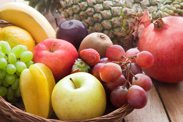 Naklejka na ściany i meble Wicker basket filled with fresh fruits against wooden background