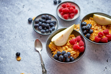 Golden cornflakes with fresh fruits of raspberries, blueberries and pear in ceramic bowl