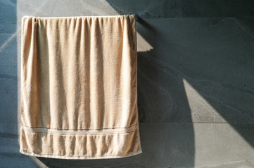Soft brown towel hanging on the grey tile wall for drying by the light of sun in the bathroom