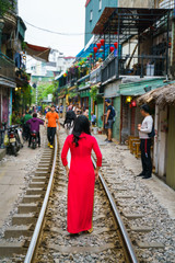 Asian girl in Vietnamese dress Ao Dai at narrow train railroad in old town in Hanoi