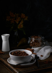 Chocolate granola in white bowl. Dark key photo style. cozy home, homemade breakfast