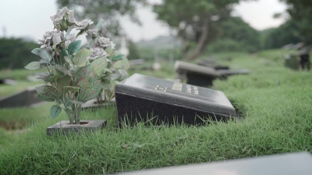 Black granite memorial plaque at cemetery and vase with artificial flowers, close up