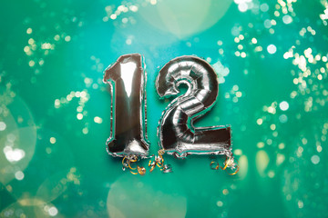 Silver Number Balloons 12 on green background with bokeh lights. Holiday Party Decoration or postcard concept with top view - obrazy, fototapety, plakaty