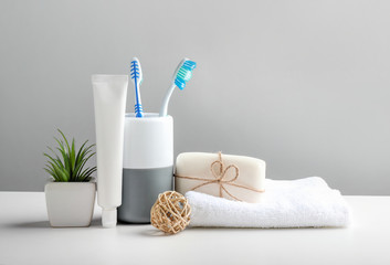 Toothbrushes in cup, toothpaste and bath towels on grey background