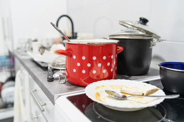 Side view on white kitchen with unwashed dirty pots and dishes on the countertop utensils and kitchen appliances in a mess after cooking