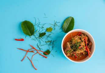 Top view, Panang pork, a popular food in Thailand put in a white cup placed on a blue background
