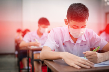 Obraz premium The Asian high school students in a white school uniform wearing the masks to do final exams in the midst of Coronavirus disease 2019 (COVID-19) epidemic and PM 2.5.