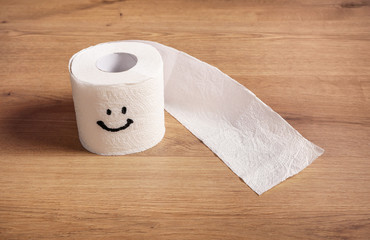 Toilet paper roll with happy smile on wooden background