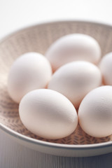 Eggs with white shells in a ceramic bowl on a white wooden table close up view