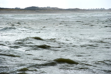 The Hague, South-Holland/Netherlands - 200226: Wild sea with waves on a stormy day with dunes and houses on the background