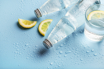 Glass water bottles, glass of water and lemon slices on blue background