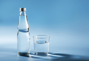 Glass water bottle and glass of water on blue background