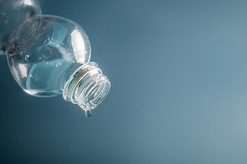 Empty plastic water bottle with last drop on blue background