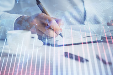 Double exposure of man's hands writing notes of stock market with forex chart.