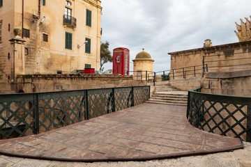 Fototapeta na wymiar A pedestrian bridge and red telephone booth at the Liesse street in Valletta near the Victoria Gate