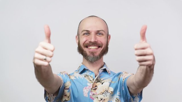 Happy bearded man wearing hawaiian shirt showing thumbs up over white background. Good job, very well. Slow Motion.