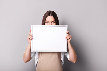 Naklejka premium Young woman in apron holding sign on gray background.