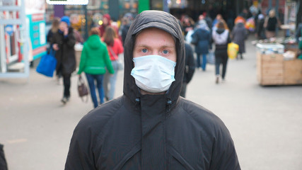 Portrait of young man with medical face mask stands at city street. Guy wearing protective mask from virus outdoor in the people crowdy. Concept of health and safety life from coronavirus and pandemic