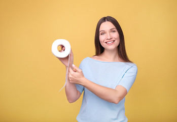 Young woman holds toilet paper on  yellow background.