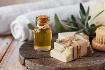 Concept of natural ingredients in cosmetology for gentle skin care. Organic olive oil in glass bottle, handmade soap bars. Atmosphere of serenity and relax. Rustic wooden background, close up.
