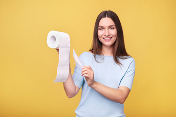 Young woman holds toilet paper on  yellow background.