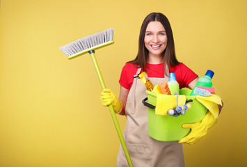Young woman in apron  on  yellow background. Cleaning concept