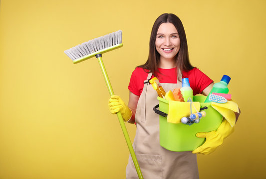 Young woman in apron  on  yellow background. Cleaning concept - Powered by Adobe