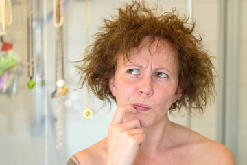 Thoughtful woman assessing her unruly tousled hair - obrazy, fototapety, plakaty