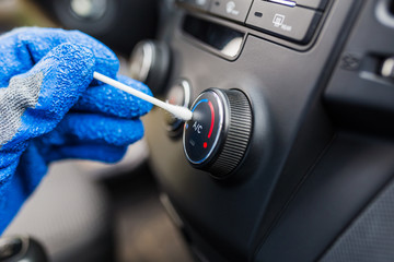 Car air conditioning disinfecting concept. Hand wearing gloves cleaning AC button with cotton swab.