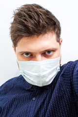 young guy caucasian in a medical mask in a blue shirt with bags under the eyes poor view. coronavirus covid 2019, quarantine