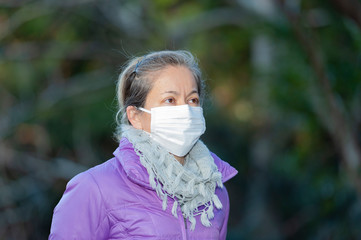 Beautiful mixed race middle aged woman wearing a white mask to protect against Coronavirus COVID-19 (SARS-CoV-2) and other infectious diseases. Side view looking up. Copy space.