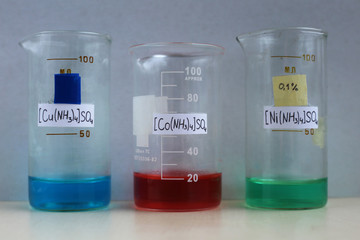 Reagents for the preparation of ammonia complexes compounds: blue copper sulfate, red cobalt sulfate, green nickel sulfate, aqueous solutions in beakers.