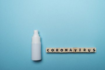 White bottle hand sanitizer with Coronavirus word written on wood block isolated over blue background. Virus outbreak prevention concept.