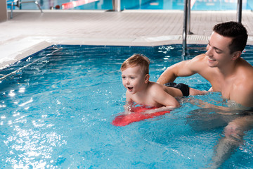 swim coach teaching happy toddler kid with flutter board in swimming pool