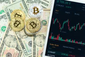 Stacks of Bitcoins on paper dollar banknotes with white modern tablet with stock market candlestick chart, virtual currency, digital crypto, metal cryptocurrency coins