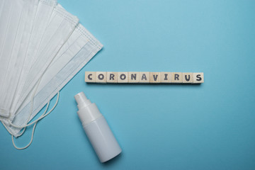 Hygienic face mask with white bottle hand sanitizer with Coronavirus word written on wood block isolated over blue background. Virus outbreak prevention concept.