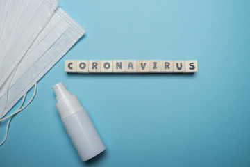 Hygienic face mask with white bottle hand sanitizer with Coronavirus word written on wood block isolated over blue background. Virus outbreak prevention concept.