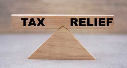 concept of the balance of words TAX win and RELIEF on wooden scales on a light background