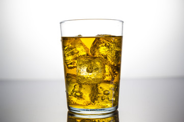 a glass of yellow drink with ice cubes