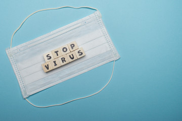 Hygienic face mask with stop virus word written on wood block isolated over blue background. Virus...