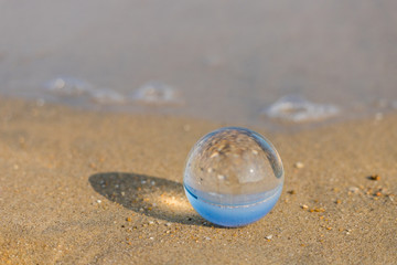 夏の海水浴場の砂浜にある透明な水晶ガラスボール