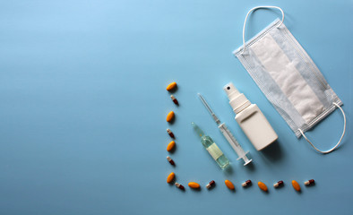 Medical mask with ampoule, syringe, antiseptic, medicines on a blue background. Covid19, coronavirus and epidemic content. Virus prevention and creating a vaccine against coronavirus. Copy space.