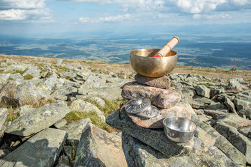 A Himalayan singing bowl and a small Zen bowl placed on stones on a top of a mountain with a view ov